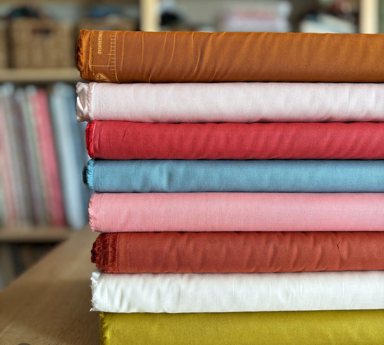 Bolts of cotton fabric in solid colors displayed neatly at The Stitching Corner, showcasing a variety of hues including red, blue, green, and yellow. 